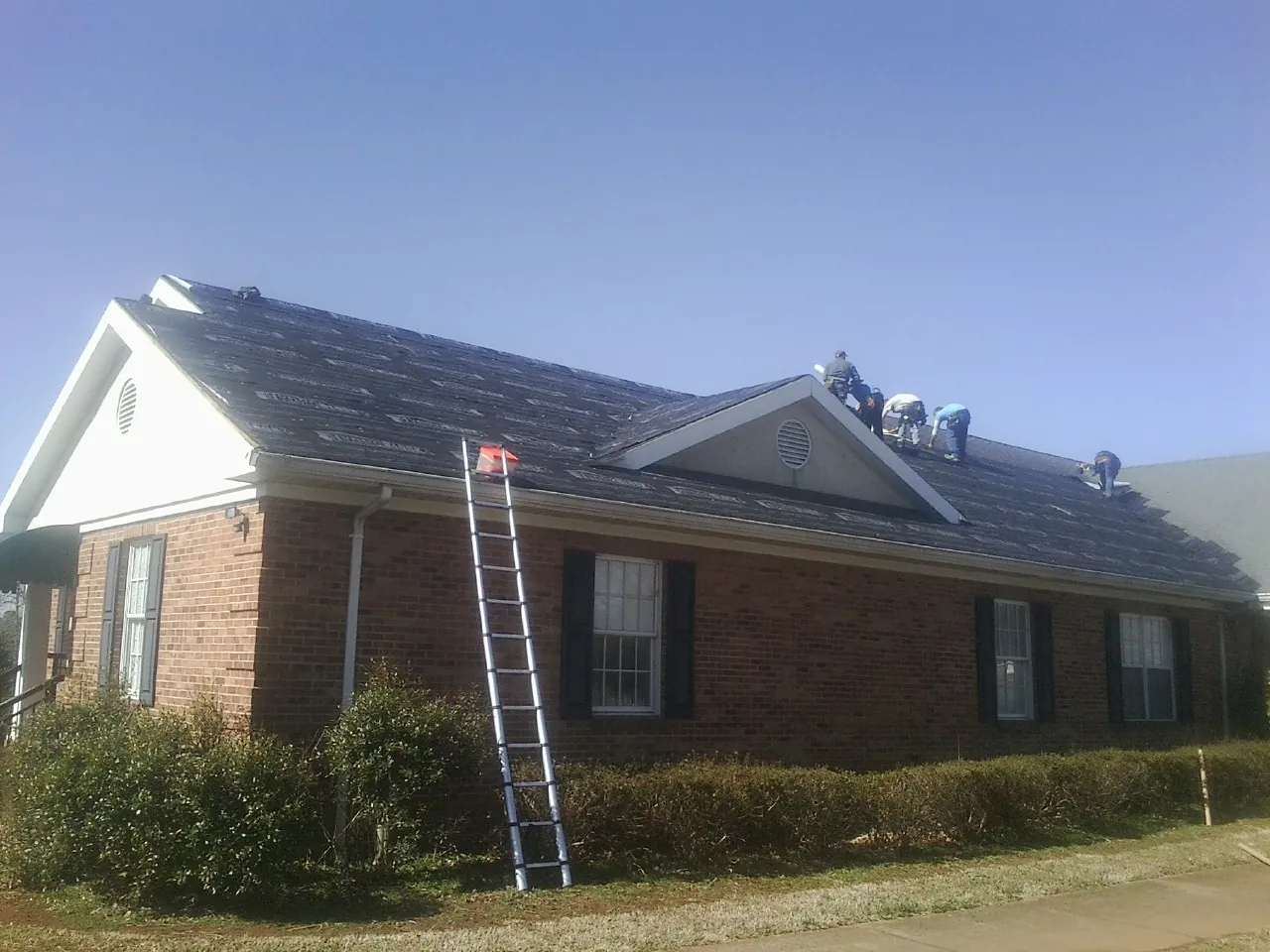 Crew tearing shingles off a brick ranch roof with a ladder set — Metal Roof Repair work by our crew in Rockledge