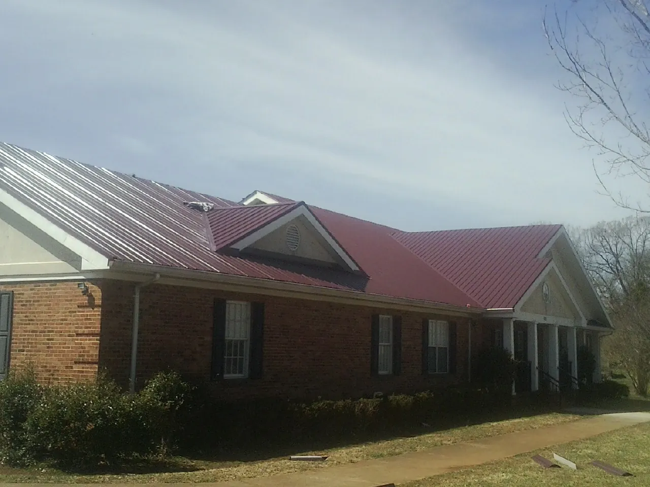 Red metal roof with gabled entries on a long brick building, from a Hail Damage Roof Repair job in Rockledge